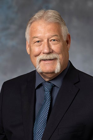 Craig Olson in a black suit, blue shirt and blue tie