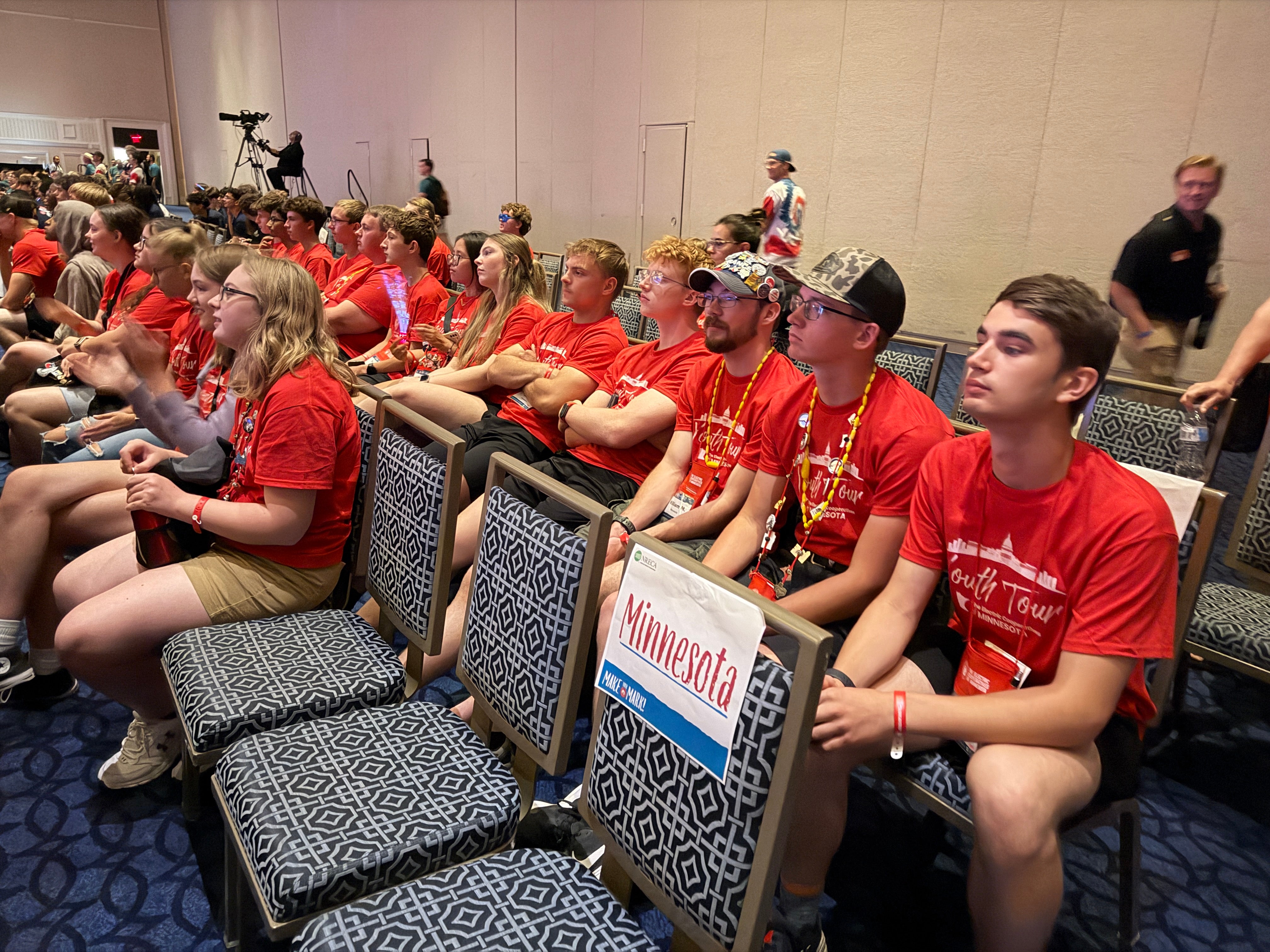 students in red shirts listening to a speaker