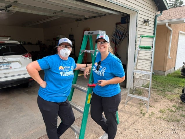 Two volunteers in blue United Way Day of Action shirts pose beside a ladder while working on a home improvement project.