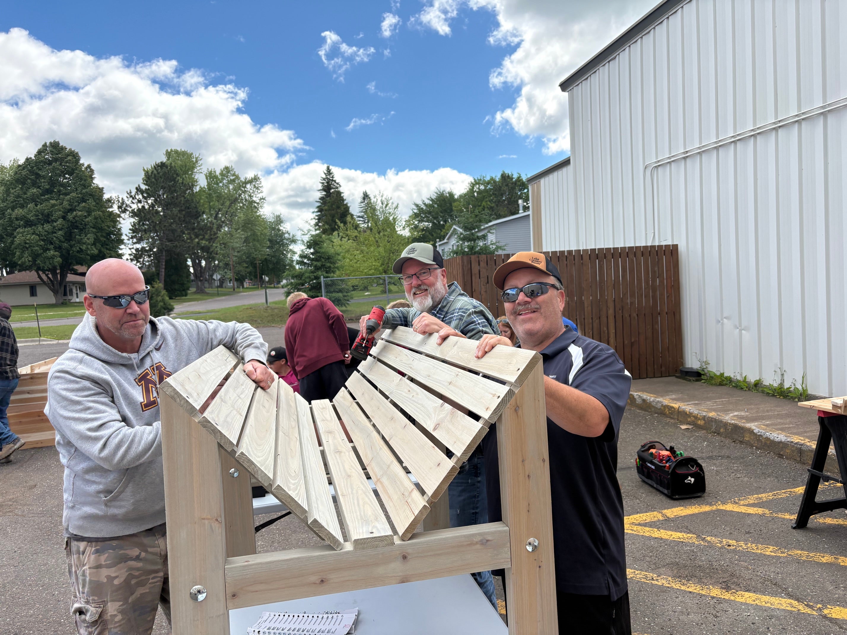 Three volunteers smile while assembling a large wooden structure during an outdoor United Way Day of Action project.