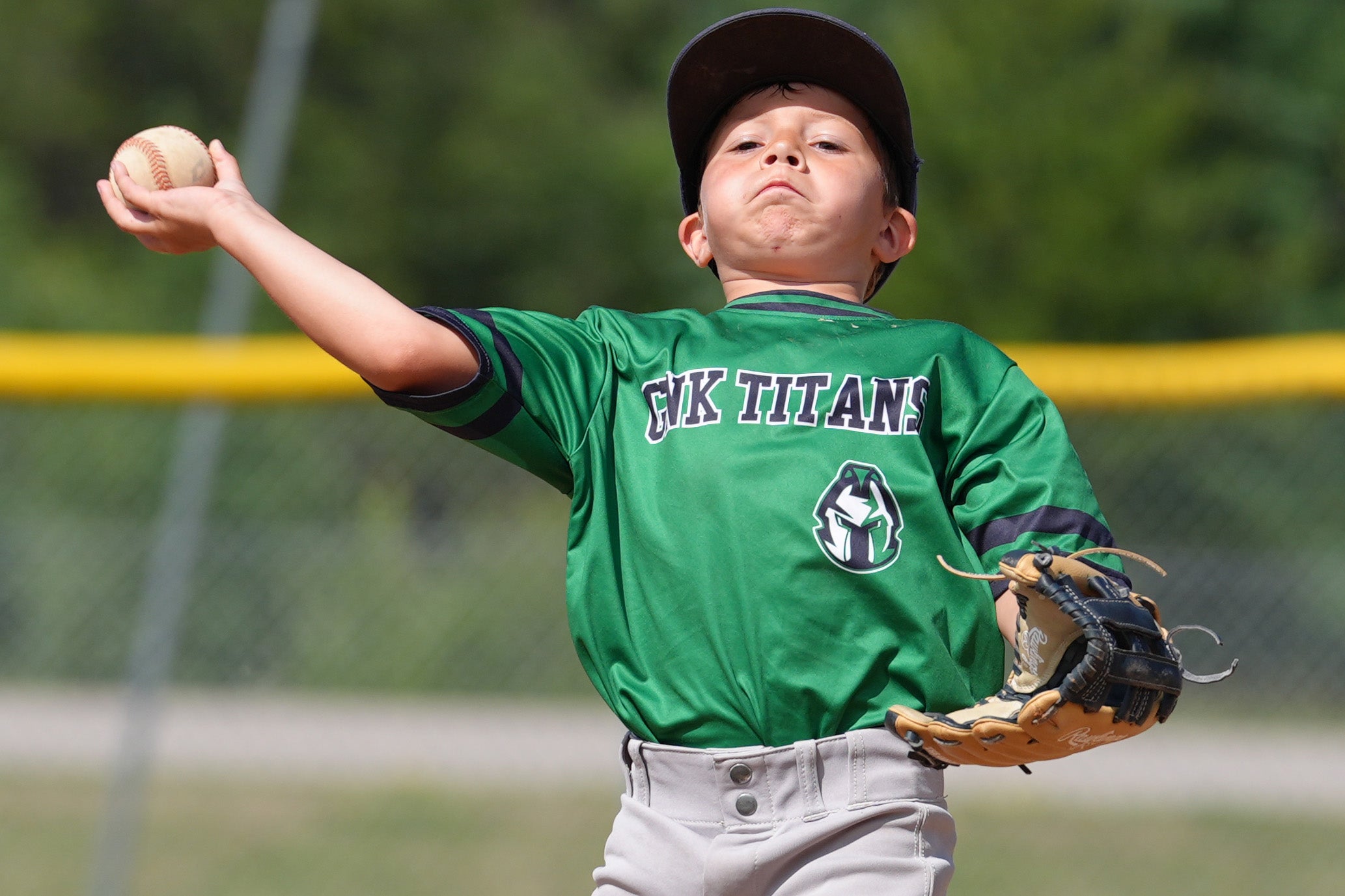 A young baseball player holds a ball near his shoulder and prepares to throw while participating in a fielding drill at an outdoor youth baseball clinic.