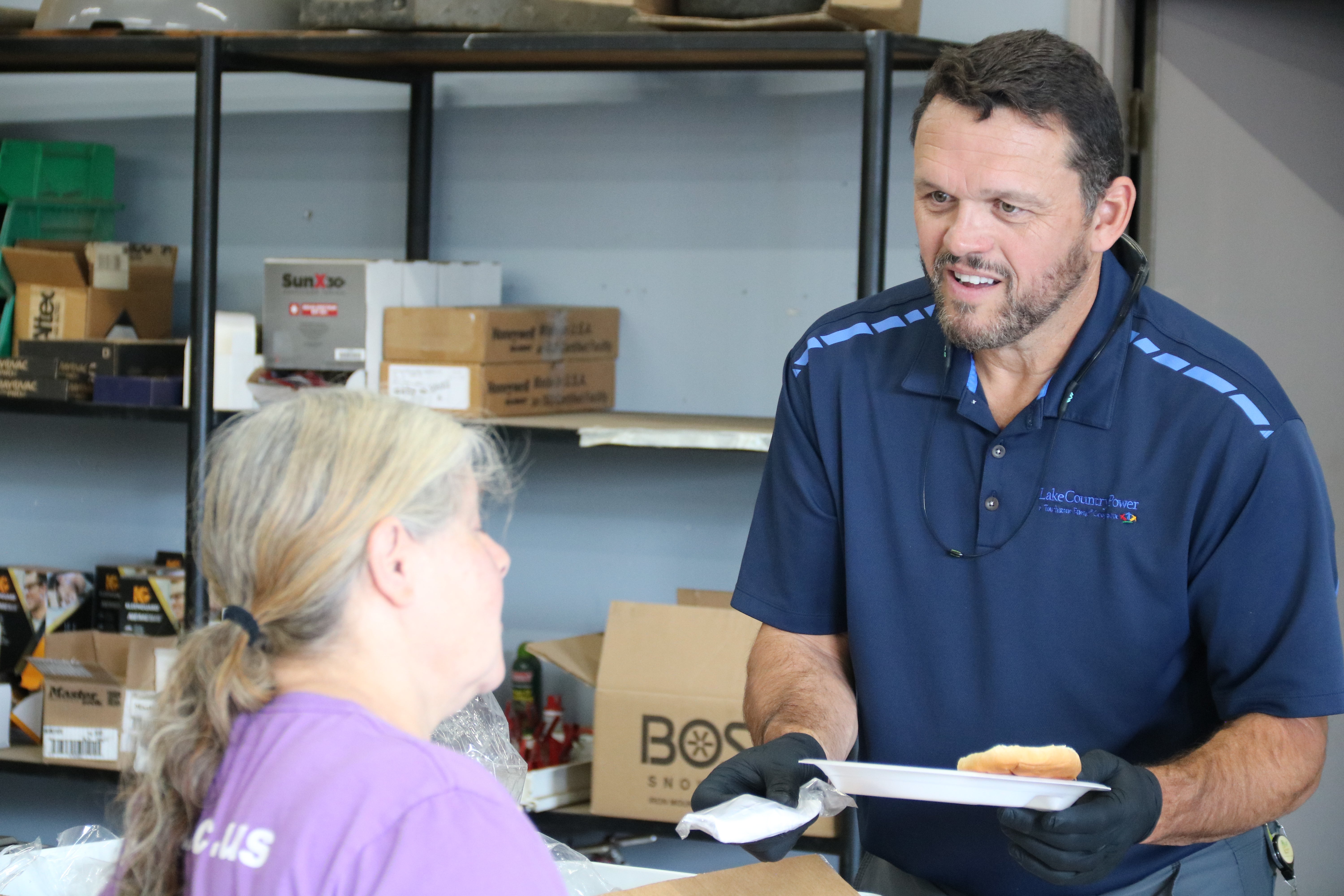 A Lake Country Power employee wearing gloves serves food to an attendee during an indoor community event.